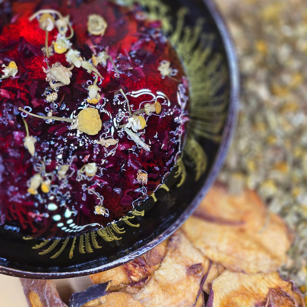 bowl of vibrant tea- hibiscus and chamomile flowers next to dried peaches